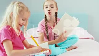 Cheerful older sister reading book for her younger sister which something drawing in notebook