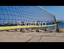 Wind blow beach volleyball net near the sunbeds and straw beach umbrellas